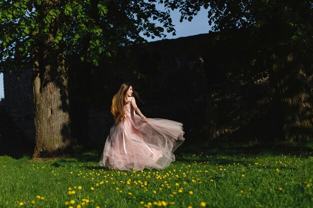 Mädchen im rosa Kleid wirbelt auf den grünen Rasen vor einer Schlosswand in den Strahlen der Abendsonne
