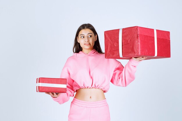 Mädchen im rosa Pyjama, das große und kleine rote Geschenkboxen hält und unzufrieden aussieht.