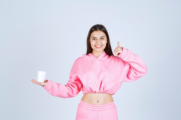 Mädchen im rosa Pyjama, der eine Kaffeetasse hält und den Geschmack genießt