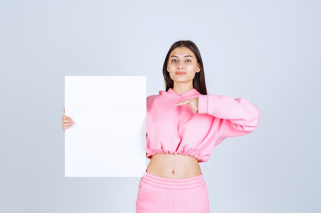 Mädchen im rosa Pyjama hält eine leere quadratische Präsentationstafel und zeigt darauf.