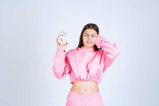 Mädchen im rosa pyjama hält einen wecker und wird wegen des lärms gestört.