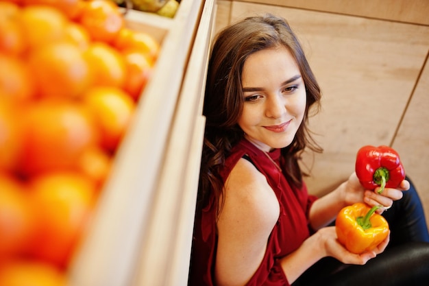 Kostenloses Foto mädchen im rot, das zwei paprika auf obstspeicher hält