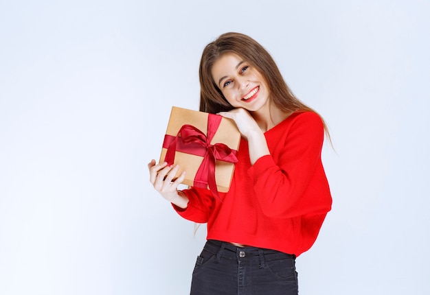 Mädchen im roten Hemd, das eine Pappgeschenkbox hält, die mit rotem Band umwickelt wird.