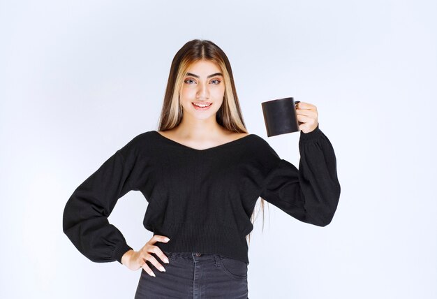 Mädchen im schwarzen Hemd, das eine schwarze Kaffeetasse hält. Foto in hoher Qualität