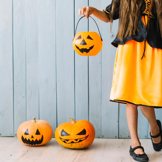 Mädchen im schwarzen und orange Kleid, das Halloween-Korb steht und hält