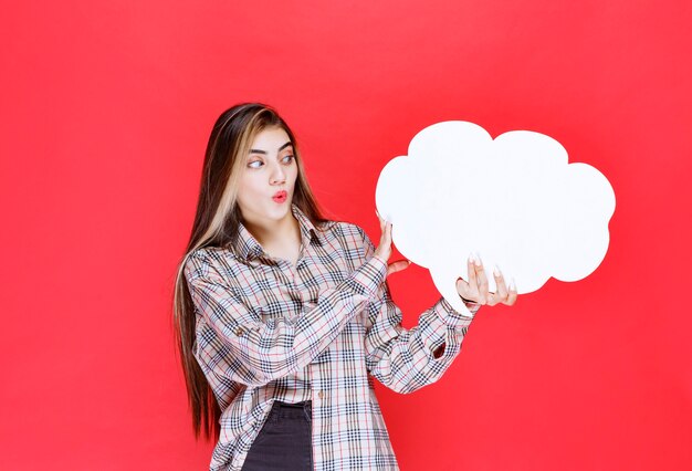 Mädchen im warmen Pullover, der ein Ideenboard in Wolkenform hält und überrascht aussieht