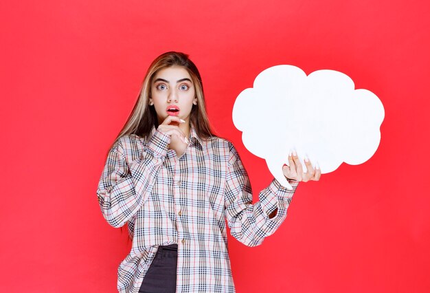 Mädchen im warmen Pullover, der ein Ideenboard in Wolkenform hält und überrascht aussieht