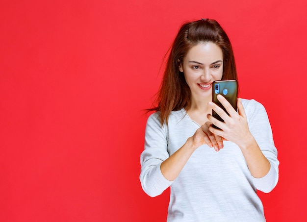 Mädchen im weißen Hemd, das ein neues Modell-Smartphone hält und einen Videoanruf tätigt oder ihr Selfie macht