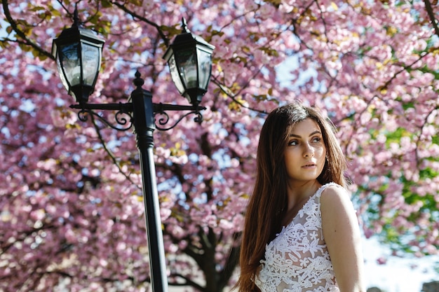 Mädchen im weißen Kleid steht unter rosa blühendem Kirschblüte-Baum im Park