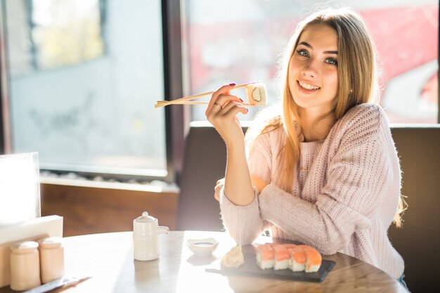 Mädchen im weißen Pullover, der Sushi zum Mittagessen an einem kleinen Kaffee isst