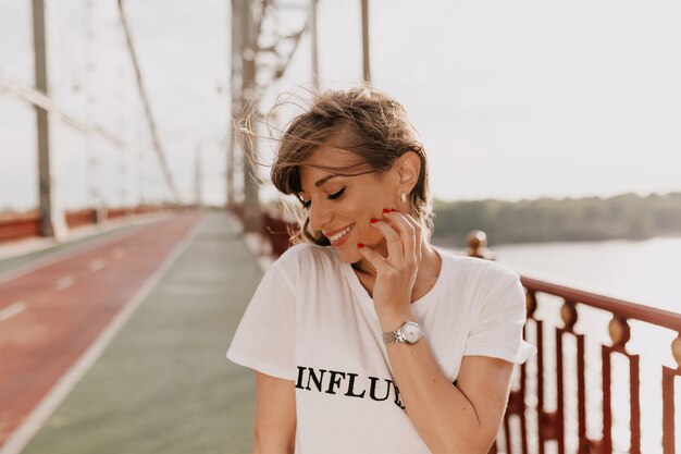 Mädchen im weißen T-Shirt, das ihr Haar berührt und Augen beim Gehen schließt