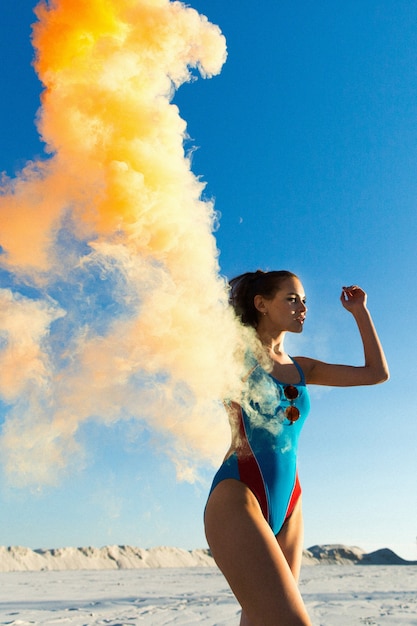 Mädchen in blau Schwimmen-Anzug Tänze mit orange Rauch am weißen Strand