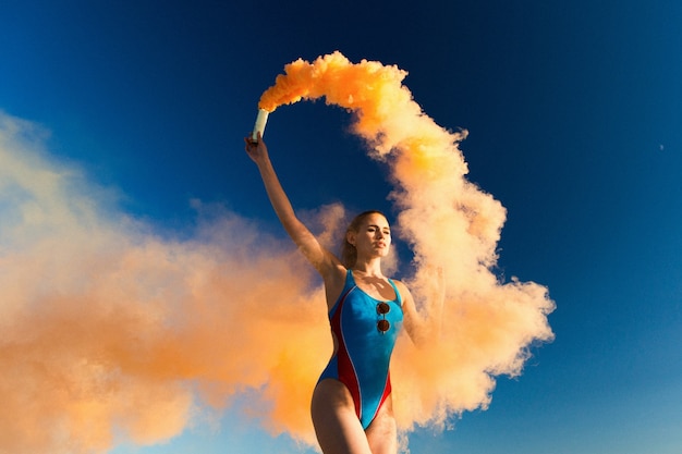 Mädchen in blau schwimmen-anzug tänze mit orange rauch am weißen strand