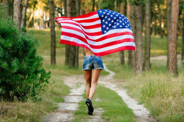 Mädchen in den denimkurzen hosen, die mit amerikanischer flagge in den händen laufen.