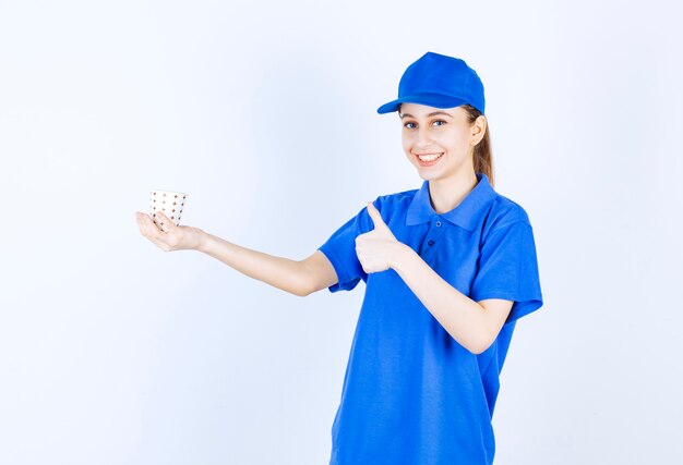 Mädchen in der blauen Uniform, die eine Einwegschale des Getränks hält und Genusszeichen zeigt.