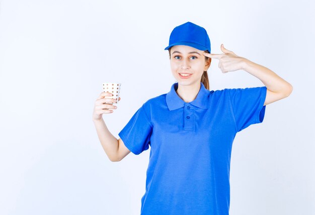Mädchen in der blauen Uniform, die eine Tasse Getränk hält und denkt oder neue Idee hat.