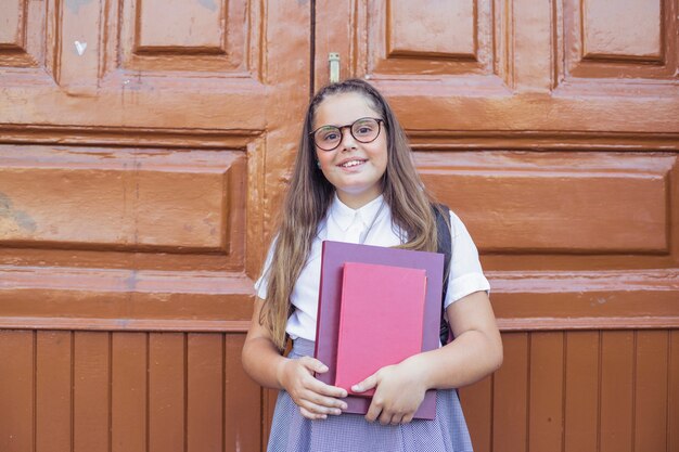 Mädchen in der Schuluniform in den Gläsern, die Bücher und das Lächeln halten