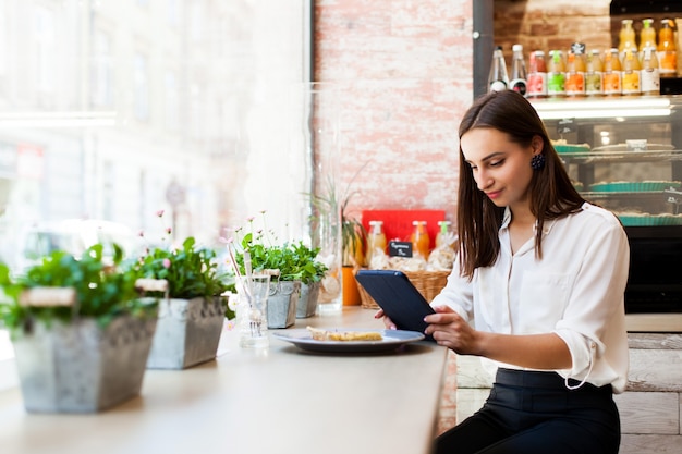 Mädchen in einem Cafe liest etwas auf dem Tablet