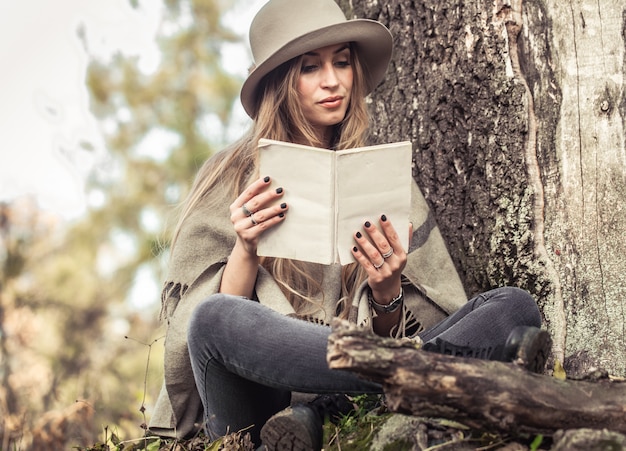 Mädchen in einem Hut, der ein Buch im Herbstwald liest