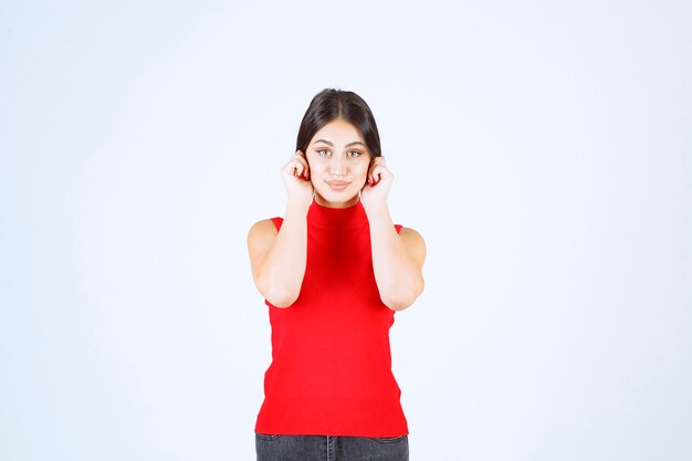 Mädchen in einem roten Hemd, das sich als Zeichen des Unglücks die Ohren zieht.