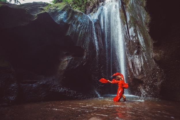 Mädchen in einem roten Kleid, das in einem Wasserfall tanzt.