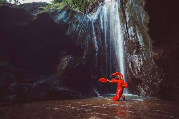 Mädchen in einem roten Kleid, das in einem Wasserfall tanzt.