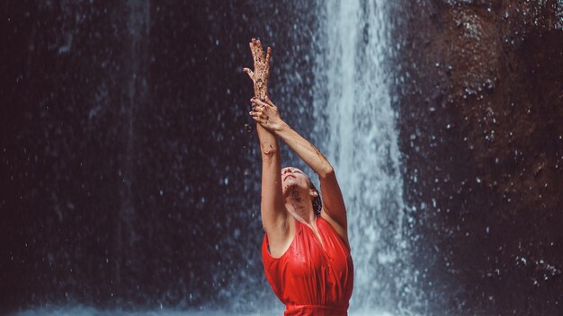 Mädchen in einem roten Kleid, das in einem Wasserfall tanzt.