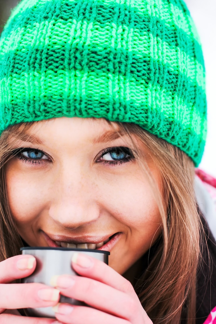 Kostenlose Foto mädchen in einer karminroten jacke und grünen hut trinken heißen tee aus einer thermoskanne in schneebedeckten bergen