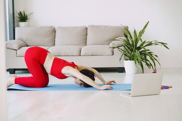 Mädchen in einer roten Sportuniform, die Yoga zu Hause praktiziert