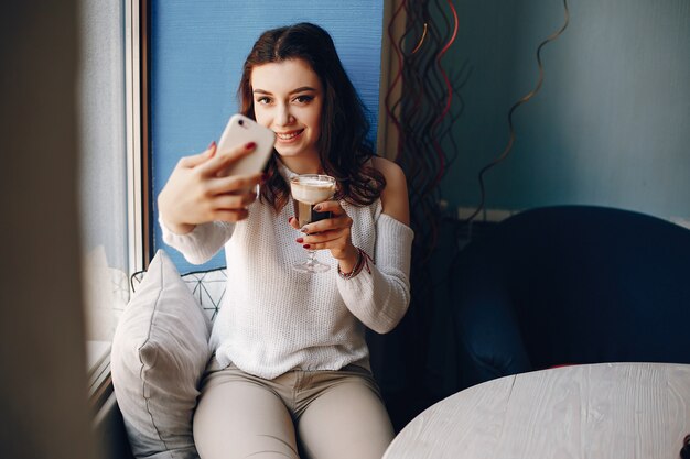 Mädchen in einer weißen Strickjacke nimmt ein selfie im Café