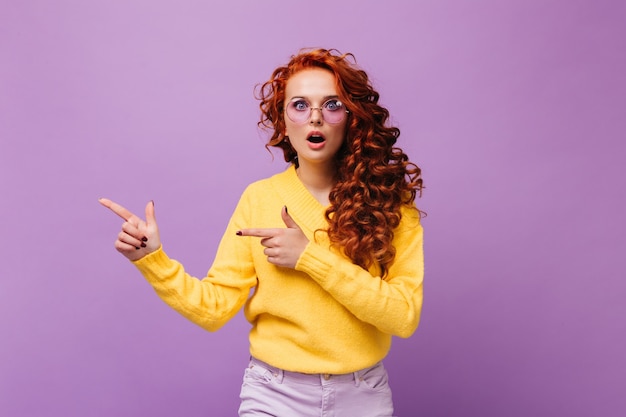 Mädchen in gelbem Pullover und lila Brille schaut überrascht in die Kamera an isolierter Wand