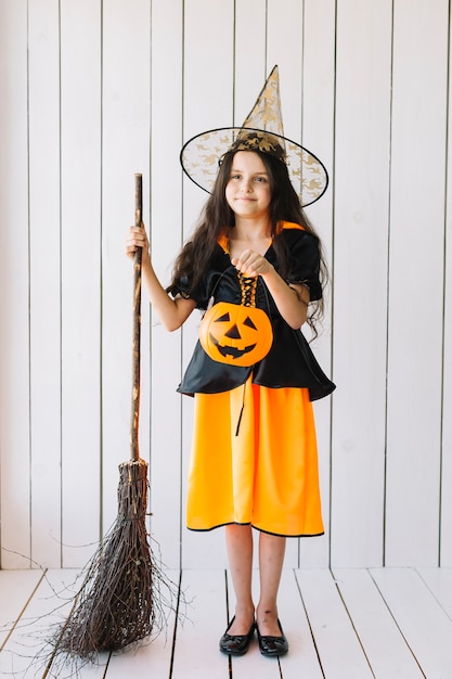 Mädchen in Halloween-Kostüm mit dem Kürbiskorb und -besen, die im Studio stehen