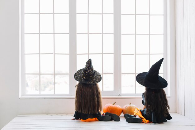 Mädchen in Halloween-Kostümen, die nahe Fenster sitzen