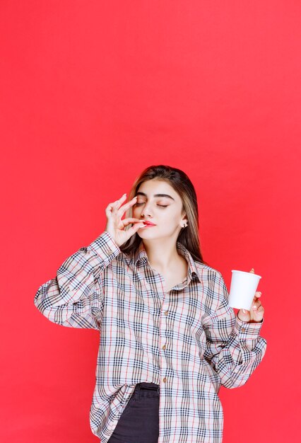 Mädchen in kariertem Hemd, das eine weiße Einweg-Kaffeetasse hält und den Geschmack genießt