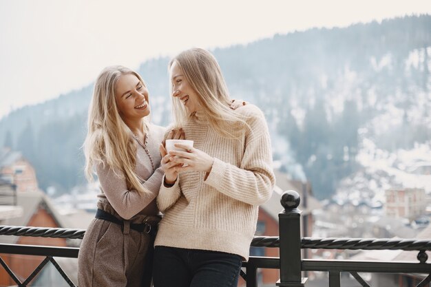 Mädchen in leichten Kleidern. Winterkaffee auf dem Balkon. Glückliche Frauen zusammen.