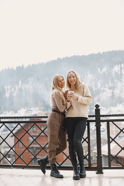 Mädchen in leichten Kleidern. Winterkaffee auf dem Balkon. Glückliche Frauen zusammen.