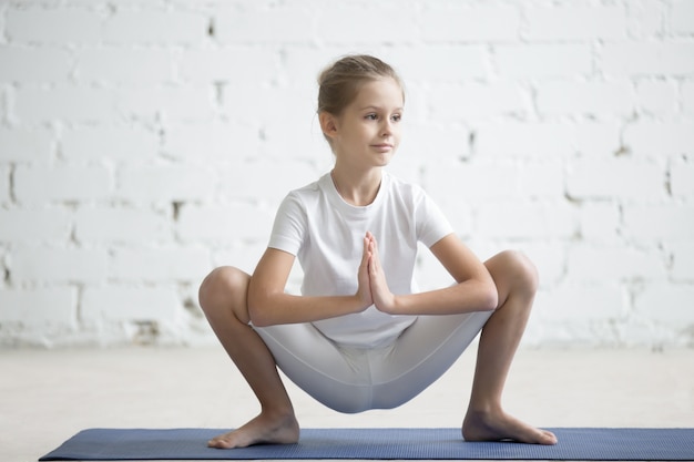 Kostenloses Foto mädchen kind in malasana pose, weiß studio hintergrund