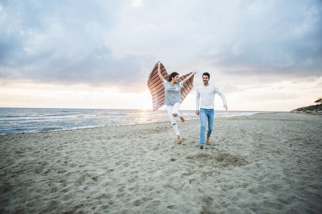 Mädchen läuft am Strand mit einer Decke und ihrem Freund neben