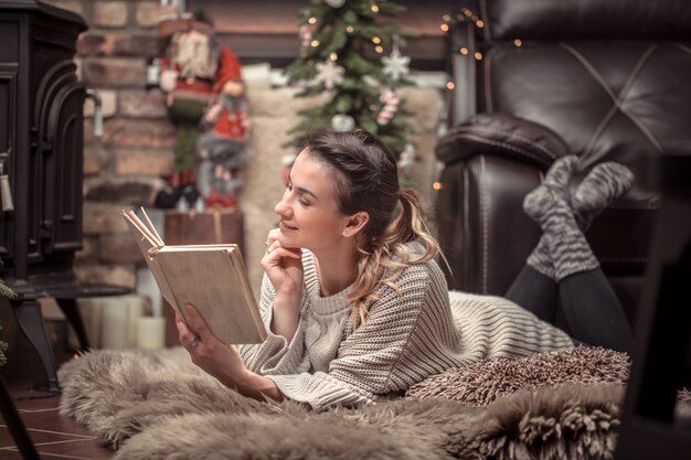 Mädchen liest ein Buch in einer gemütlichen häuslichen Atmosphäre in der Nähe des Kamins