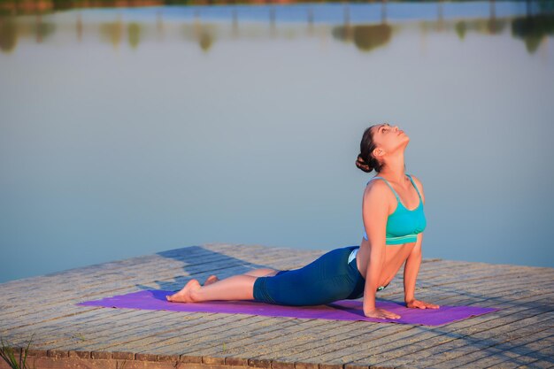 Mädchen macht Yoga-Übungen am Flussufer bei Sonnenuntergang