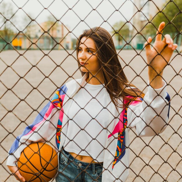 Mädchen mit Basketball hinter Zaun