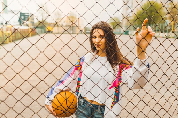 Mädchen mit Basketball hinter Zaun