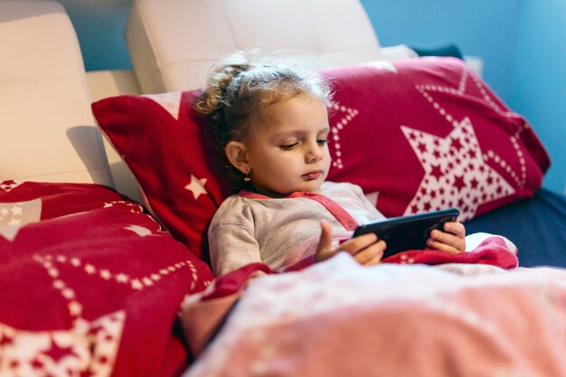 Mädchen mit dem Smartphone, der im Bett sich entspannt