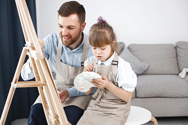 Mädchen mit Down-Syndrom und ihr Vater malen auf einer Staffelei mit Pinseln