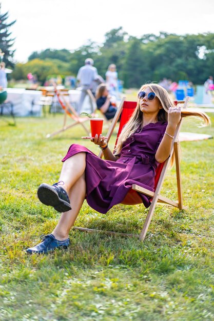 Mädchen mit einem Smartphone und einem Cocktail in der Natur in einem Liegestuhl. Ruhetag im Sommer.