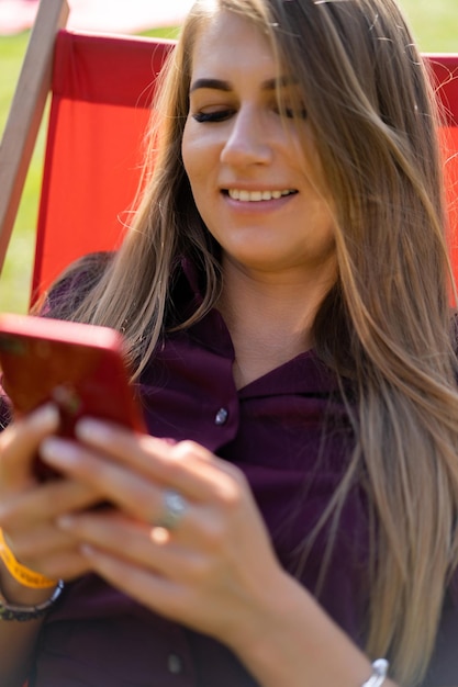 Mädchen mit einem Smartphone und einem Cocktail in der Natur in einem Liegestuhl. Ruhetag im Sommer.