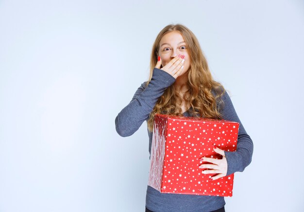 Mädchen mit einer roten Geschenkbox sieht aufgeregt und überrascht aus.