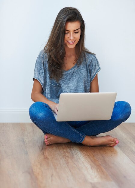 Mädchen mit gekreuzten Beinen, das ihren Laptop benutzt