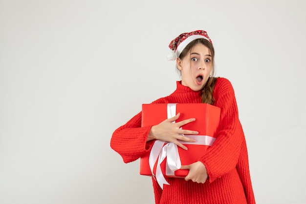 Mädchen mit großen Augen und Weihnachtsmütze, das ihr Weihnachtsgeschenk auf Weiß hält