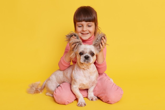 Mädchen mit Hund, der zusammen spielt, hebt die Ohren des Welpen und lacht auf gelb